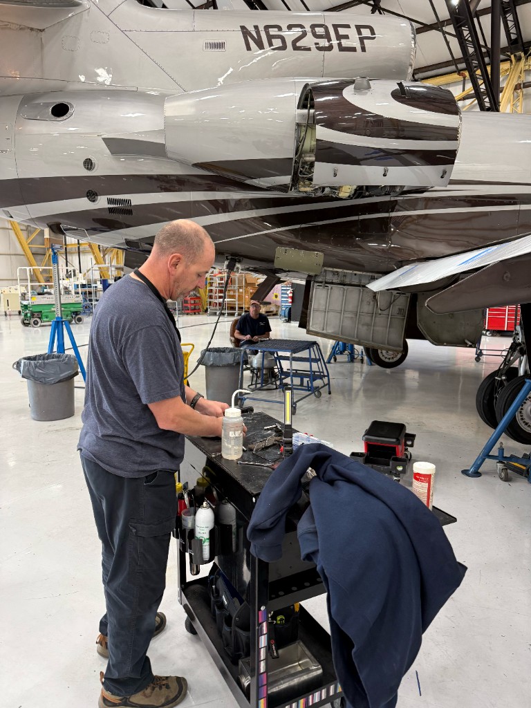 Technician at a work cart under a business jet with cowlings open